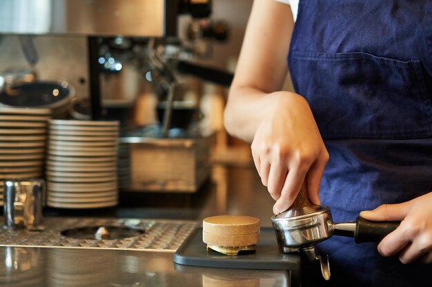 Close up of barista female hands pressing coffee into tamper prepares order in cafe behind counter