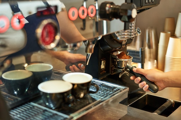 Foto gratuita primo piano della mano del barista e della macchina da caffè con chicchi macinati freschi lavorano nella caffetteria