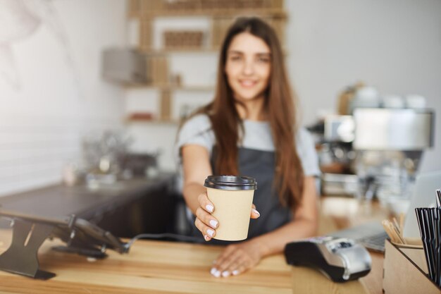 顧客にカップを行くためにコーヒーを提供するバリスタのクローズアップ