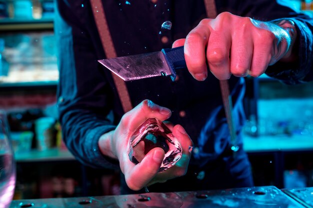 Close up of barman crushing a big piece of ice on the bar counter with a special bar equipment on it for a cocktail