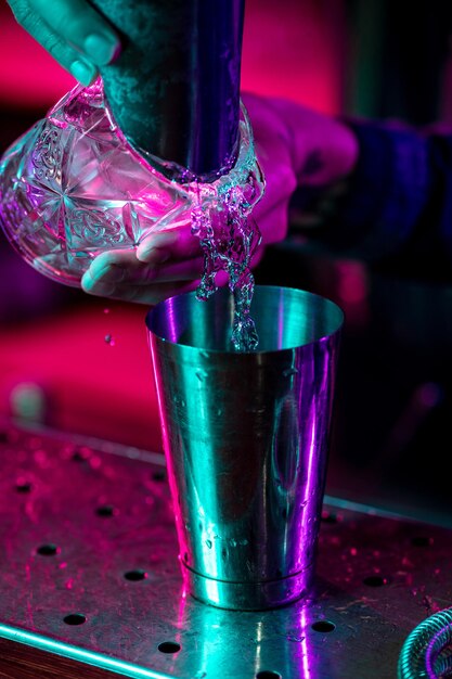 Close up of barman finishes preparation of alcoholic cocktail, pouring drink in multicolored neon light