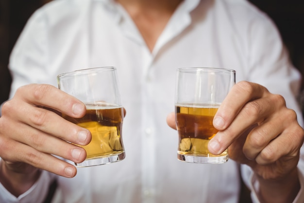 Free photo close-up of bartender holding whisky shot glasses at bar counter