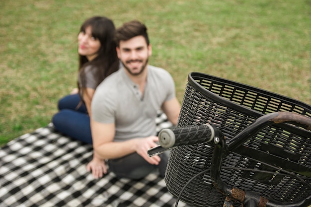 Close-up of basket on bicycle in front of young couple sitting in the park