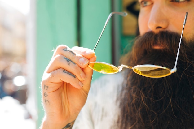 Close-up of beard man holding yellow eyeglasses in sunlight