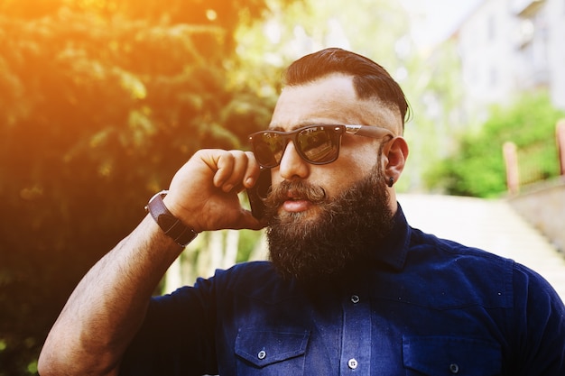 Крупным планом бородатый человек разговаривает по телефону