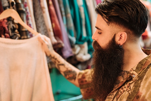 Free photo close-up of a bearded young man choosing t-shirt from the store