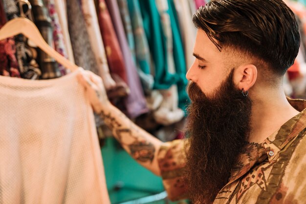 Close-up of a bearded young man choosing t-shirt from the store