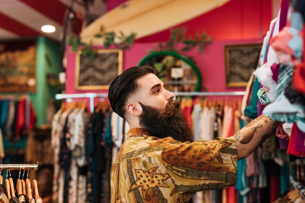 Free photo close-up of bearded young man looking at clothes hanging on rail