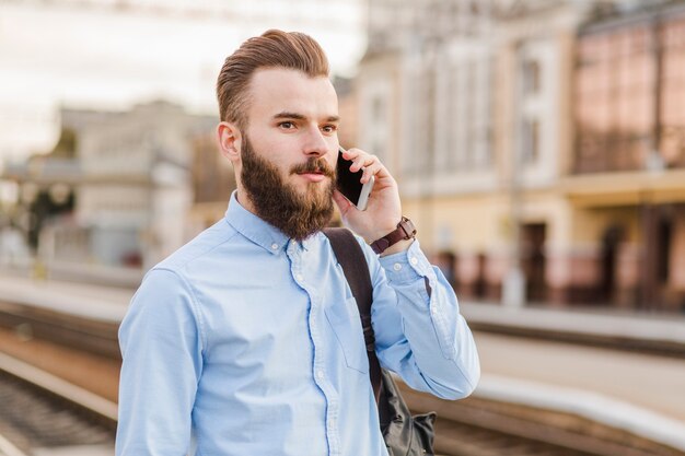 鉄道駅で携帯電話を使用してひげのある若い男のクローズアップ