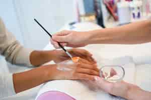 Free photo close-up of beautician applying cream on woman's hand using brush.