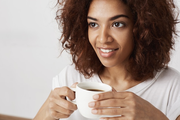 Закройте вверх красивой африканской девушки усмехаясь держащ чашку кофе.