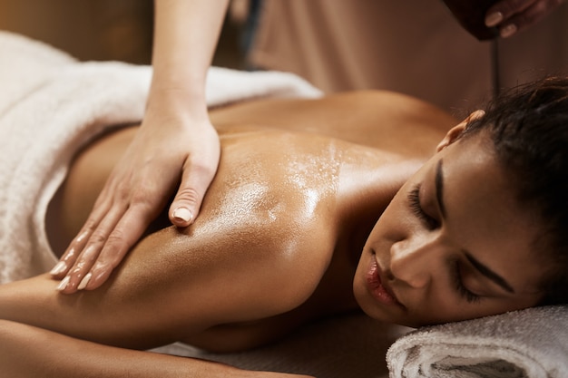 Close up of beautiful african woman enjoying massage in spa salon.