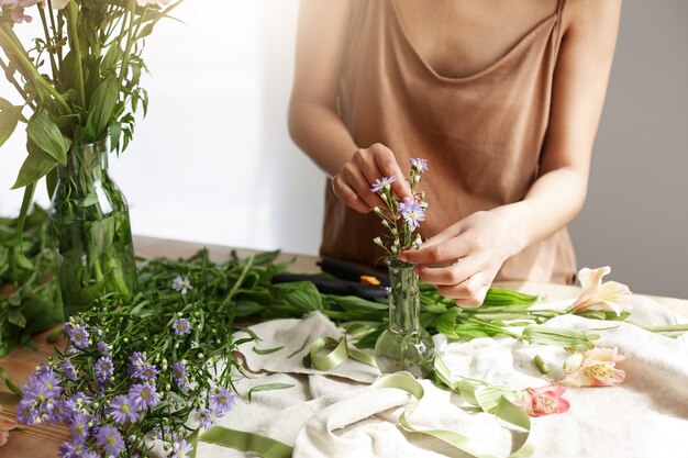 Close up of beautiful african woman florist making bouquet in flower shop over white wall.