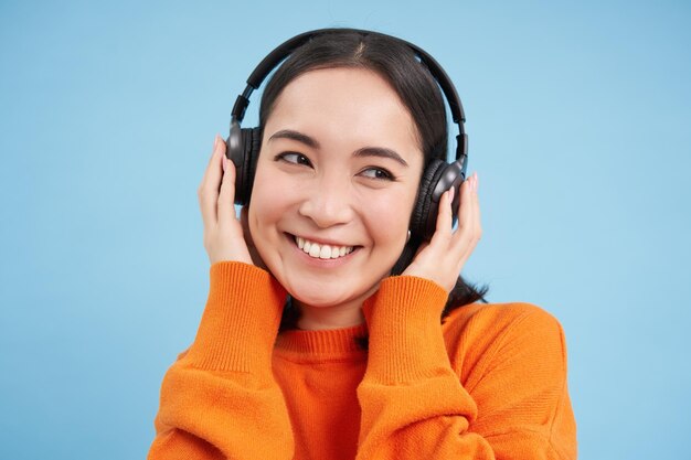 ヘッドフォンで美しいアジアの女性のクローズ アップ笑顔し、音楽を聴くポッド キャストを楽しんで立っています。