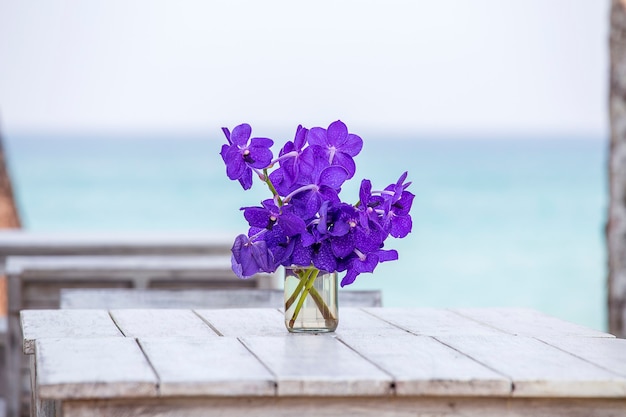海​の​近く​の​白い​木製​の​テーブル​に​青い​蘭​の​花​の​美しい​花束​を​閉じます​。​タイ