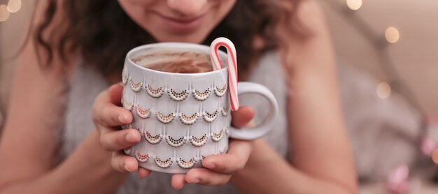 Close-up of a beautiful Christmas cup in female hands on a blurred background.