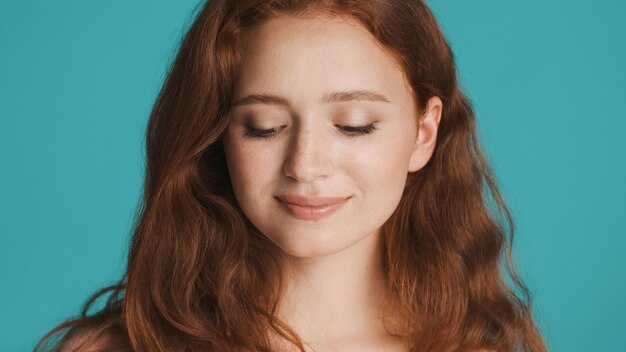 Close up beautiful cute redhead girl dreamily posing on camera over colorful background