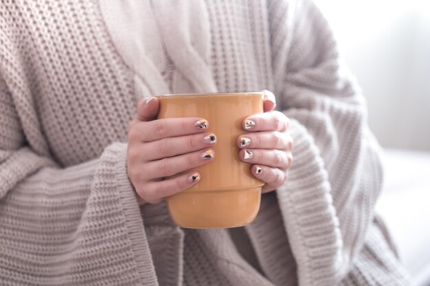 Close up of beautiful female hands holding big white cup of cappuccino coffee and flowers