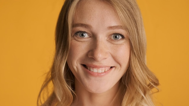 Close up beautiful smiling blond girl joyfully looking in camera over colorful background