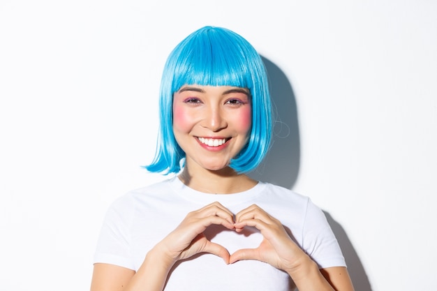 Free photo close-up of beautiful smiling woman in blue wig, celebrating halloween, showing heart gesture, standing.