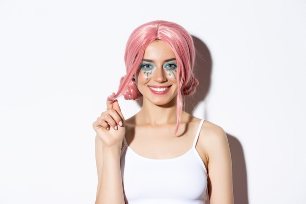 Close-up of beautiful smiling woman in pink wig, celebrating holiday, looking happy at camera, standing.