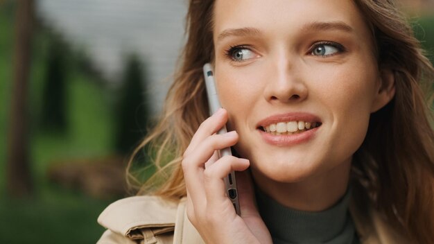 Close up beautiful student girl talking with best friend on phone while resting in park