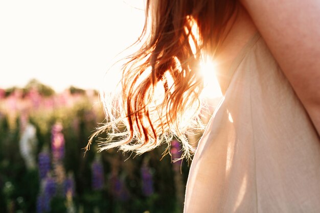 close up of beautiful woman lock of hair on sunset background in flower field. 