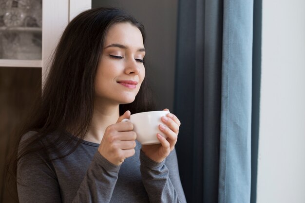 一杯のコーヒーを楽しんでいるクローズアップの美しい若い女性