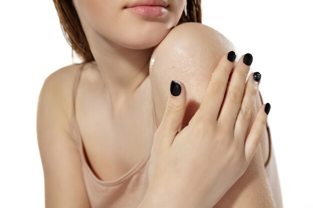 Close up of beautiful young woman massaging skin with moisturizer on white