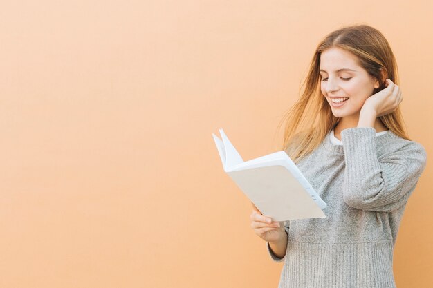 色付きの背景に対して本を読んで美しい若い女性のクローズアップ