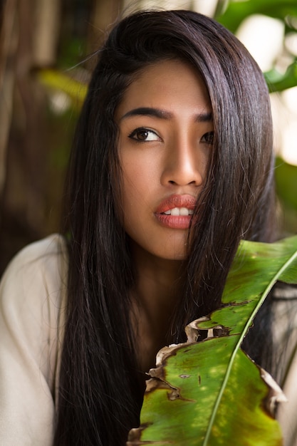 Close up beauty portrait of asian woman with perfect skin posing in tropical garden. Healthy hairs, full lips.