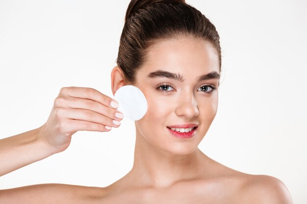 Close up beauty portrait of brunette attractive woman cleaning her face with cotton pad