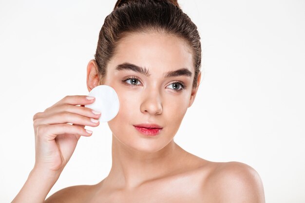 Close up beauty portrait of brunette attractive woman cleaning her face with cotton pad