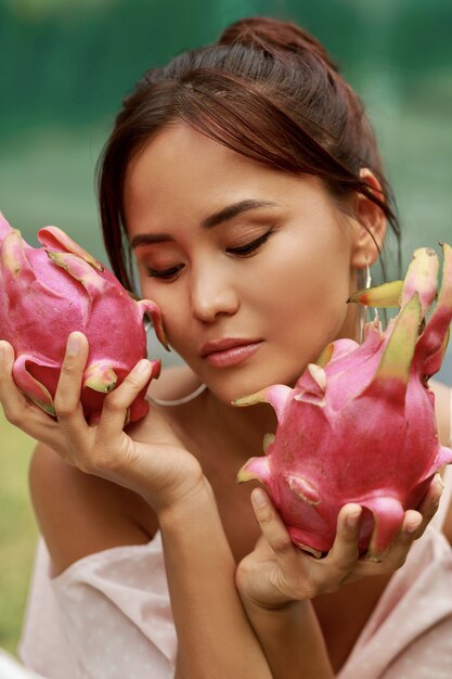 Close up beauty portrait of pretty Asian woman with dragon fruit next to face.