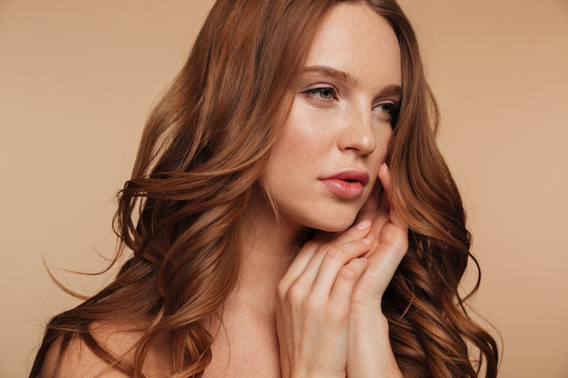 Free photo close up beauty portrait of pretty ginger woman with long hair looking away while posing with arms near face