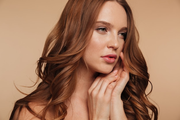 Close up Beauty portrait of pretty ginger woman with long hair looking away while posing with arms near face