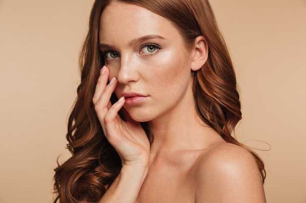 Close up Beauty portrait of sensual ginger woman with long hair posing with arm near face while looking