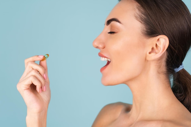 Free photo close-up beauty portrait of a topless woman with perfect skin and natural make-up, holding a supplement, vitamin omega 3, fish oil, on a turquoise background