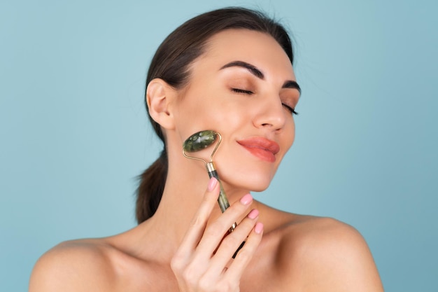 Close up beauty portrait of a woman with perfect skin and natural make-up, plump nude lips, holding a roller massager for face and neck