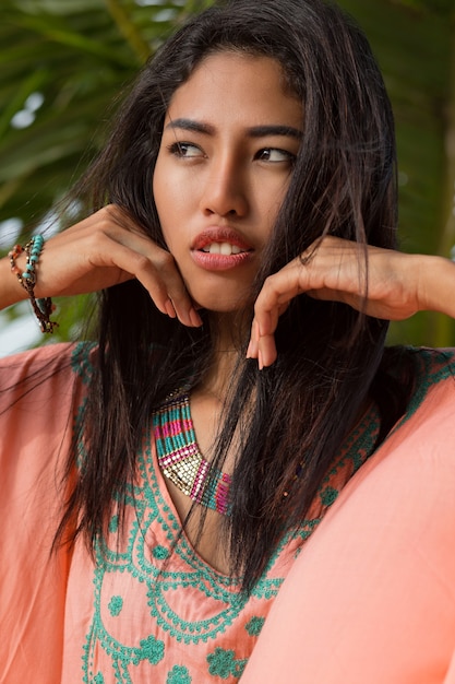 Close up beauty portrait of young asian woman on palm tree. Perfect skin. Looking to the ocean. Sunset.