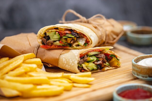 Close up of beef burrito with tomato cucumber lettuce jalapeno served with fries and sauces