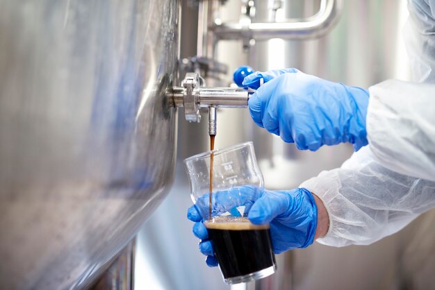 醸造所でのビール充填ガラスのクローズアップと技術者による品質管理