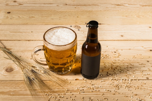 Close-up of beer in glass and bottle with ears of wheat on wooden background