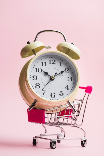 Close-up of big alarm clock on trolley over pink background