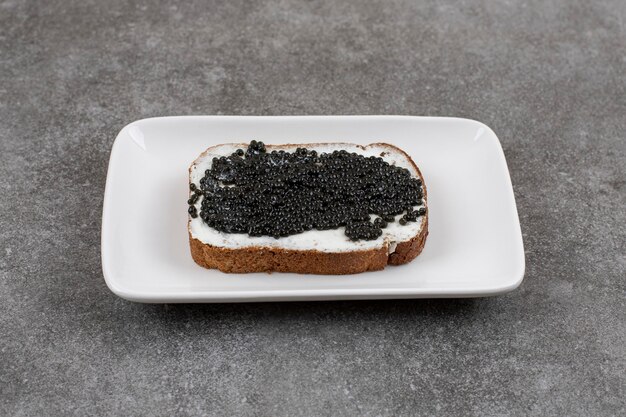 Close up of black caviar sandwich on white plate on grey surface