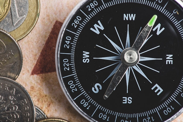 Close-up of black compass with some coins