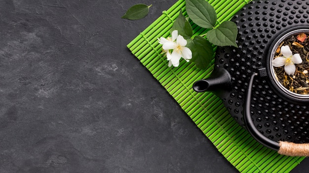 Free photo close-up of black teapot with dried tea herb on green placemat over textured background