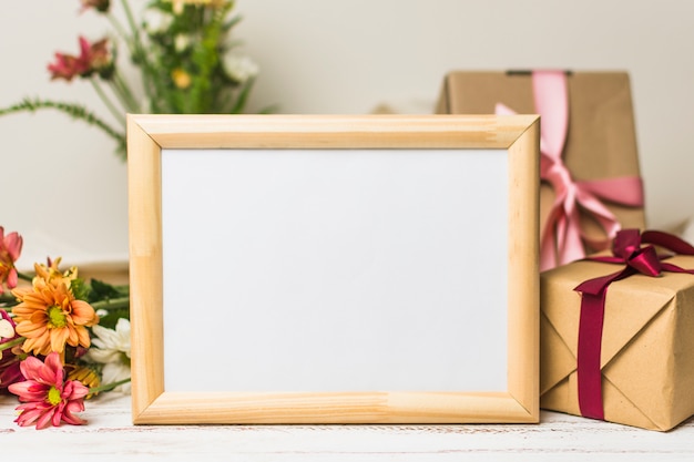 Close-up of blank wooden frame with gift and flowers