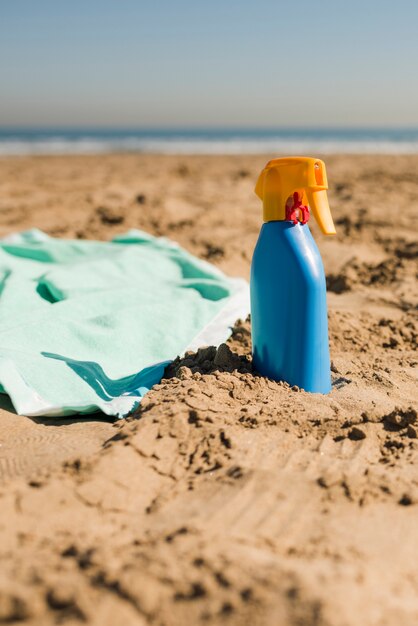 Close-up of blanket and sunscreen cream blue bottle on the sand beach