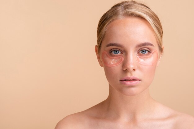 Close-up blonde woman with eye pads looking at camera 